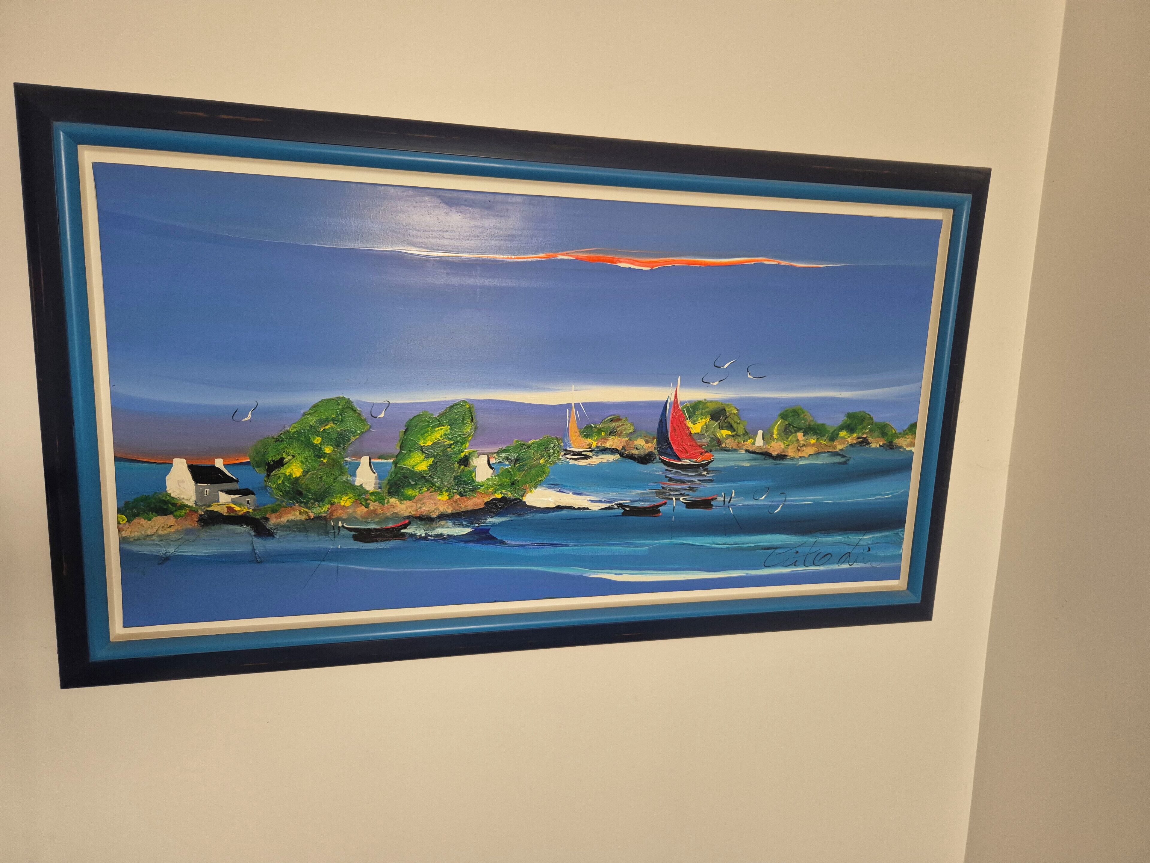 A framed painting of a coastal scene with houses, trees, and boats.