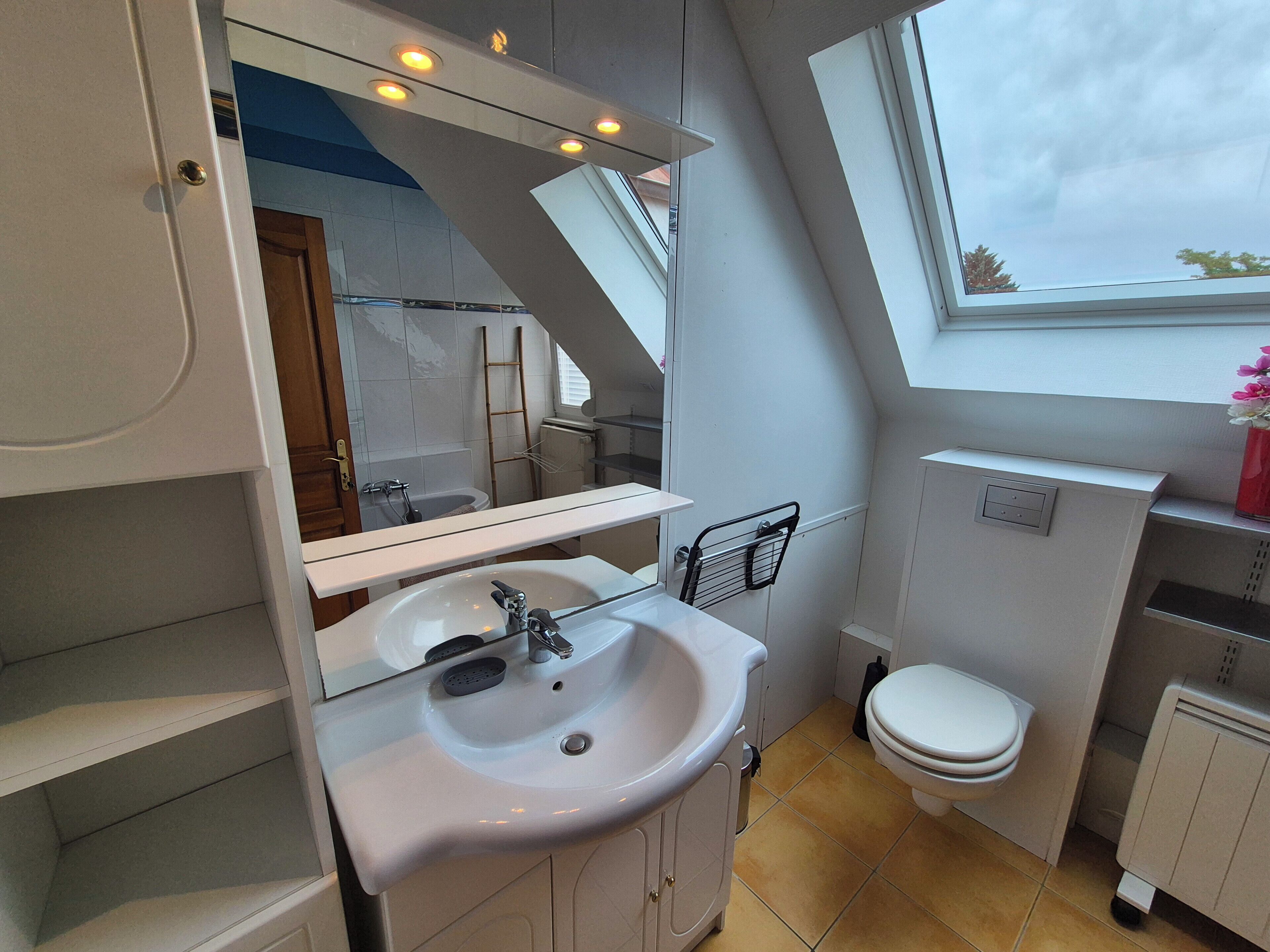 A modern bathroom with a skylight, a white sink, a toilet, and a mirror.