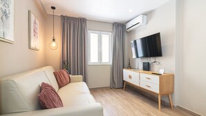 Ett modernt vardagsrum med en soffa, en tv, ett träskåp och ett fönster med gardiner.