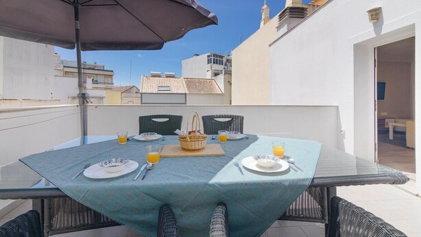 A rooftop terrace with a table set for two, a wicker chair, and a large umbrella. - Elsa's House, Algarve, Faro (Faro)