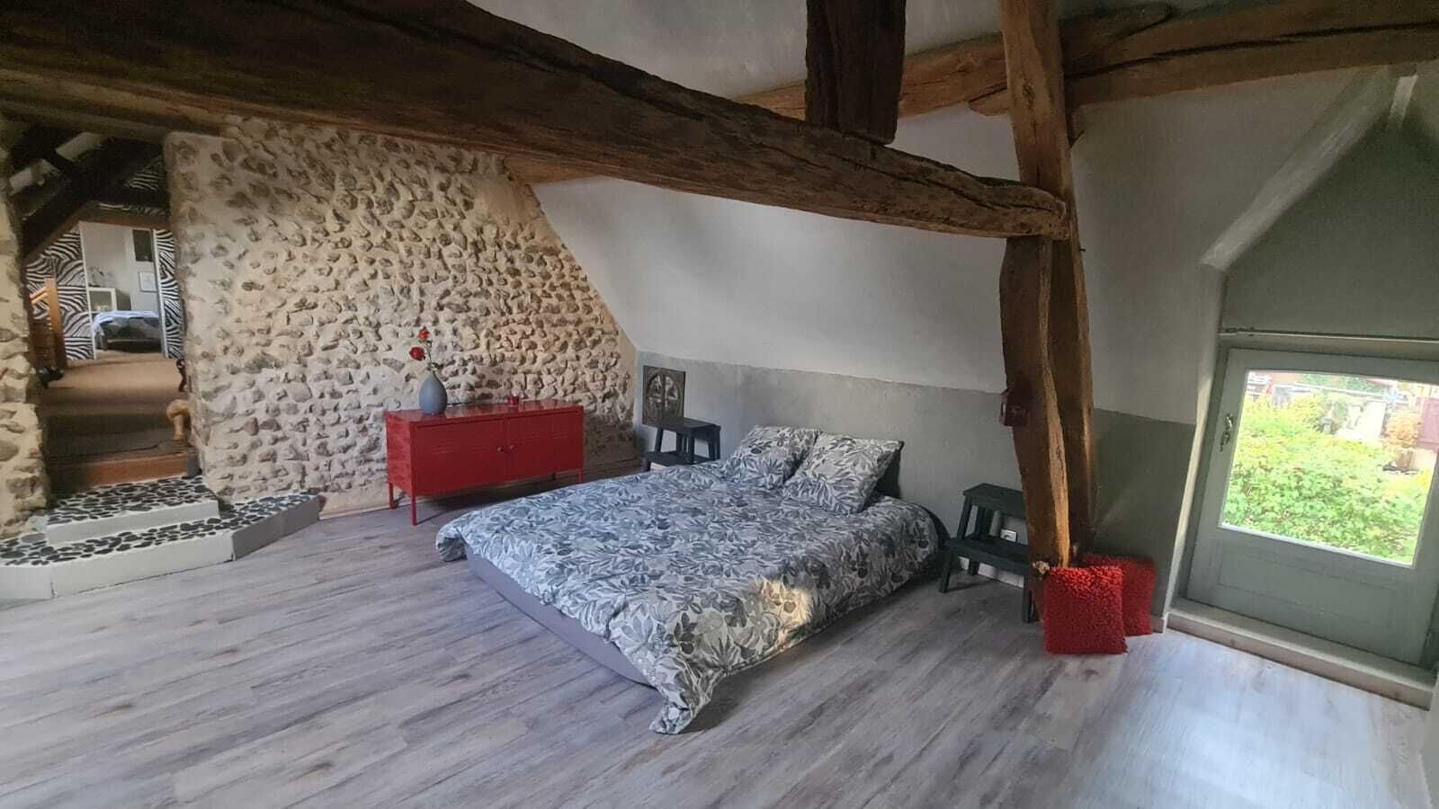 A bedroom with a stone wall, a bed, a red dresser, and a window with a view.