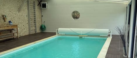 Una piscina interior con suelo de baldosas, un banco y una escalera adosada a la pared.