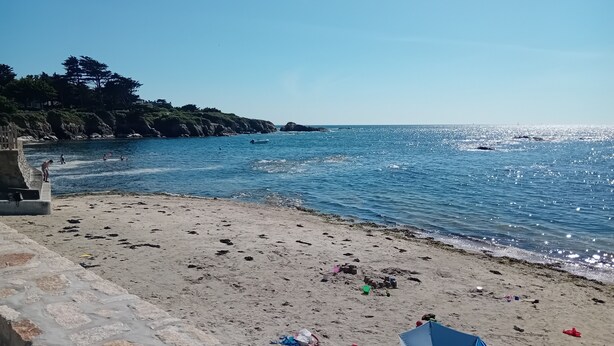 Una spiaggia con un muro di pietra, un ombrellone blu e arancione e oggetti sparsi sulla sabbia.