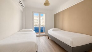 A hotel room with two single beds, a large window with a view of buildings, and a ceiling-mounted air conditioning unit. - Apartment with a terrace in Cannes (Cannes)