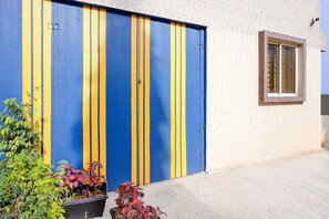 Ein Gebäude mit einer blau-gelb gestreiften Garagentür, einem Fenster mit braunem Rahmen und Blumentöpfen im Vordergrund.