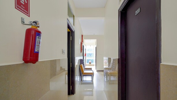 A hallway with a fire extinguisher mounted on the wall, a door labeled '205', and a view into a room with a window. - Classic Red Cherry Wagtail (Bengaluru)