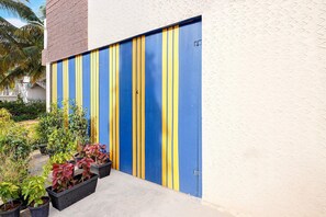 Ein Gebäude mit einer blau-gelb gestreiften Garagentür, Blumentöpfen davor und blauem Himmel.