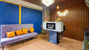 A hotel reception area with a purple sofa, a chandelier, and a sign that reads 'HOTELO OYO-Serviced.' - Classic Red Cherry Wagtail (Bengaluru)