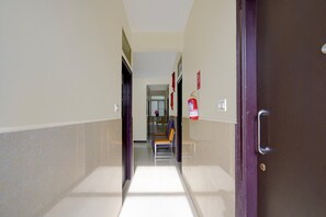 A corridor with a fire extinguisher mounted on the wall, a door on the right, and a bench in the distance. - Classic Red Cherry Wagtail (Bengaluru)