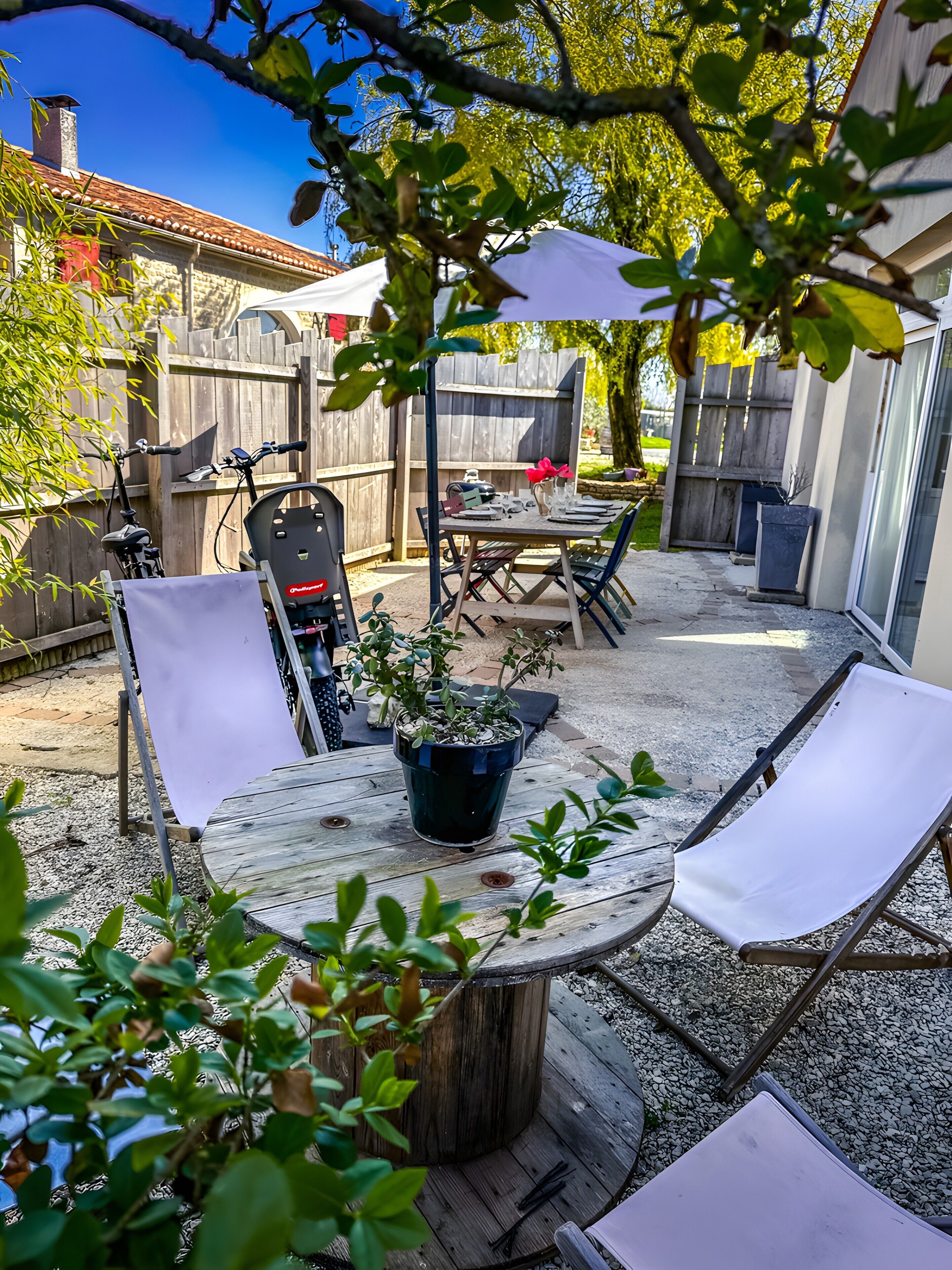 Une terrasse extérieure avec une table ronde, des chaises, un pot de fleurs et un vélo.