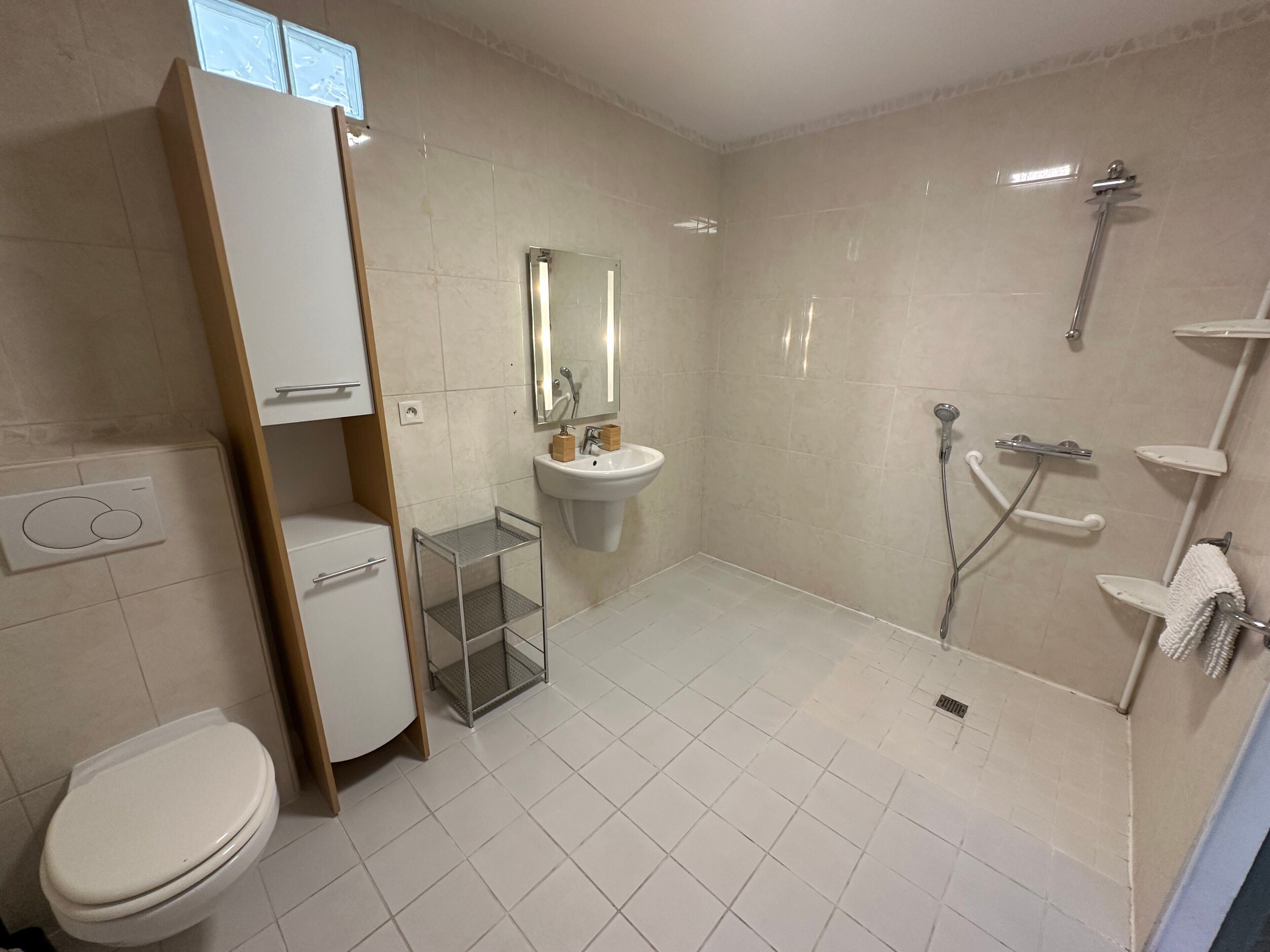 Ein modernes Badezimmer mit Toilette, Waschbecken, Dusche und einer kleinen Ablagefläche.
