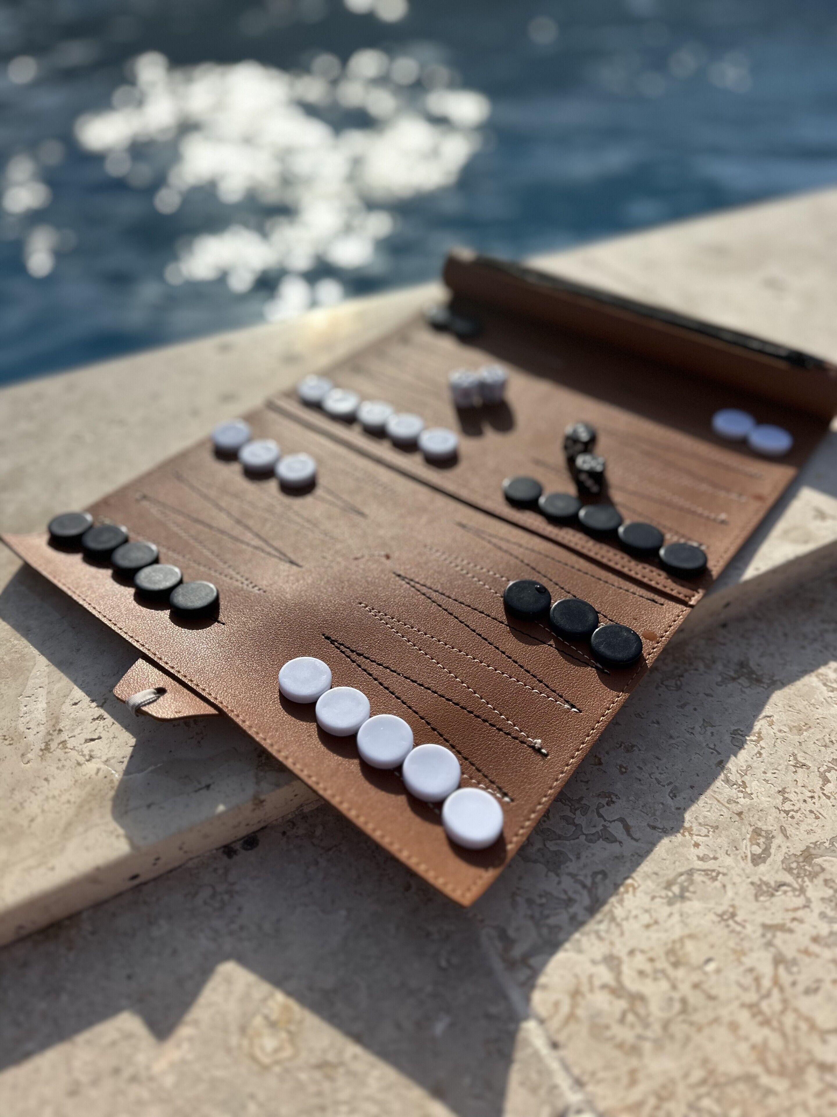 Un jeu de société en bois dont les pièces sont disposées sur une surface en pierre, près d’une étendue d’eau.