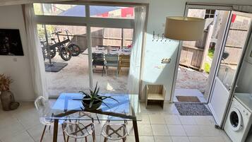 A room with a glass table, chairs, a potted plant, a washing machine, and a view of a patio with a motorcycle and outdoor furniture.