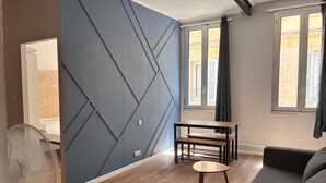 A modern living room with a blue accent wall, a wooden floor, a sofa, a small table, and a standing fan. - Charming flat in Avignon shopping streets (Avignon)