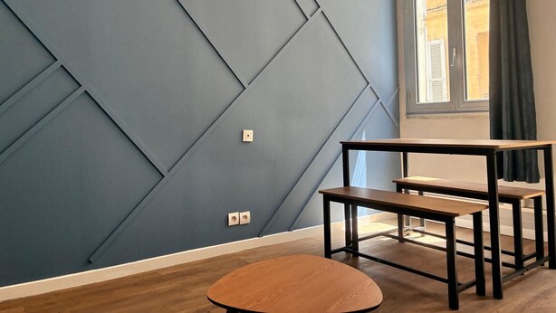 A room with a geometric-patterned wall, a window with curtains, and a wooden table with benches. - Charming flat in Avignon shopping streets (Avignon)