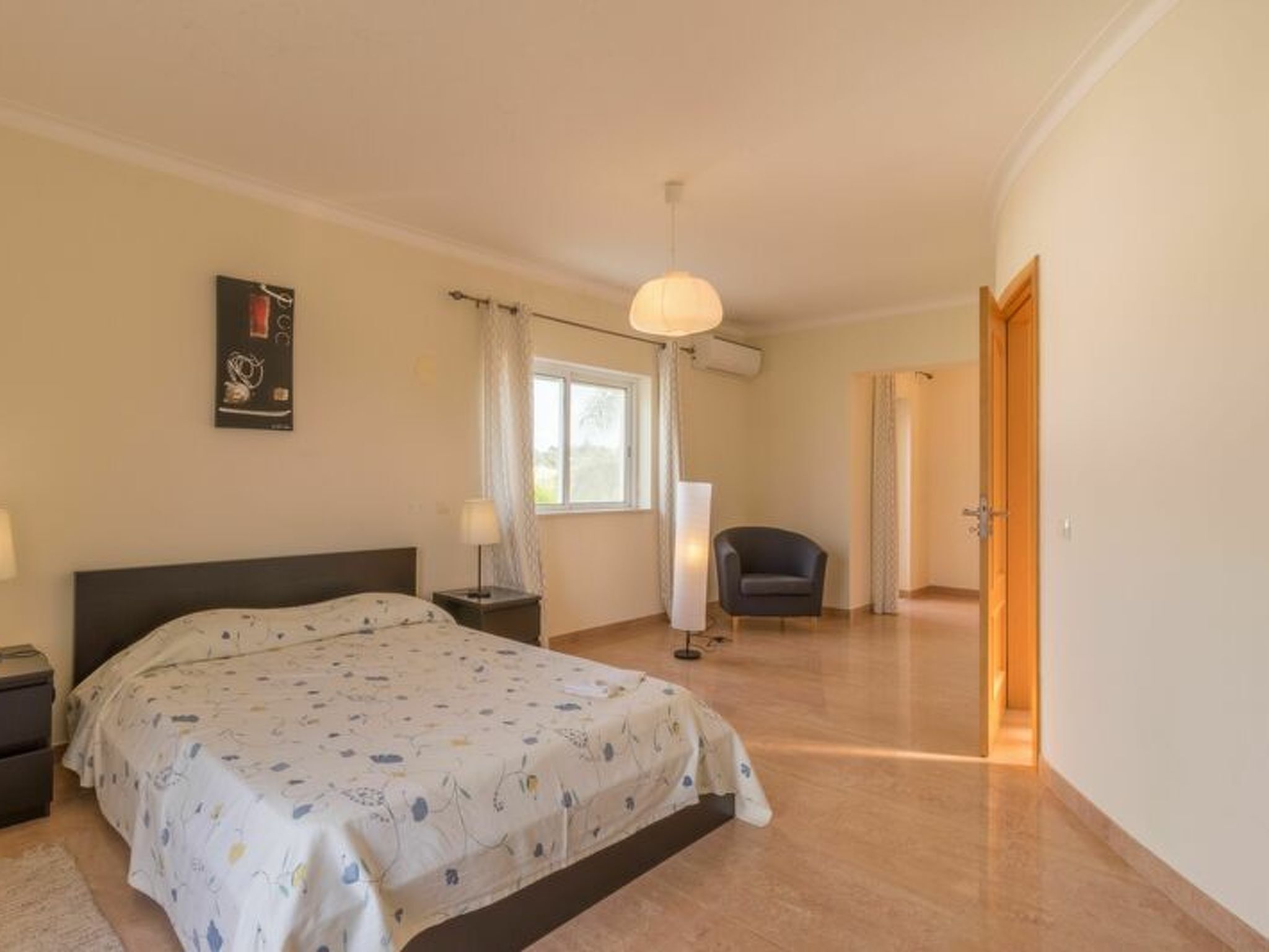 Un dormitorio con cama, mesitas de noche, una silla, una ventana con cortinas y un equipo de aire acondicionado.
