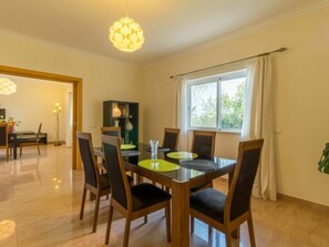 A dining area with a table and chairs, a hanging light fixture, a window with curtains, and a door leading to another room. - V5 Alvor by Interhome (Alvor)