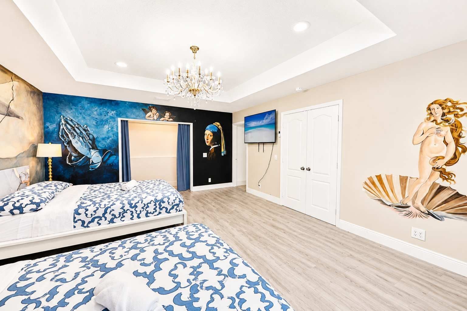 A bedroom with a bed, a chandelier, a TV, and a mural.