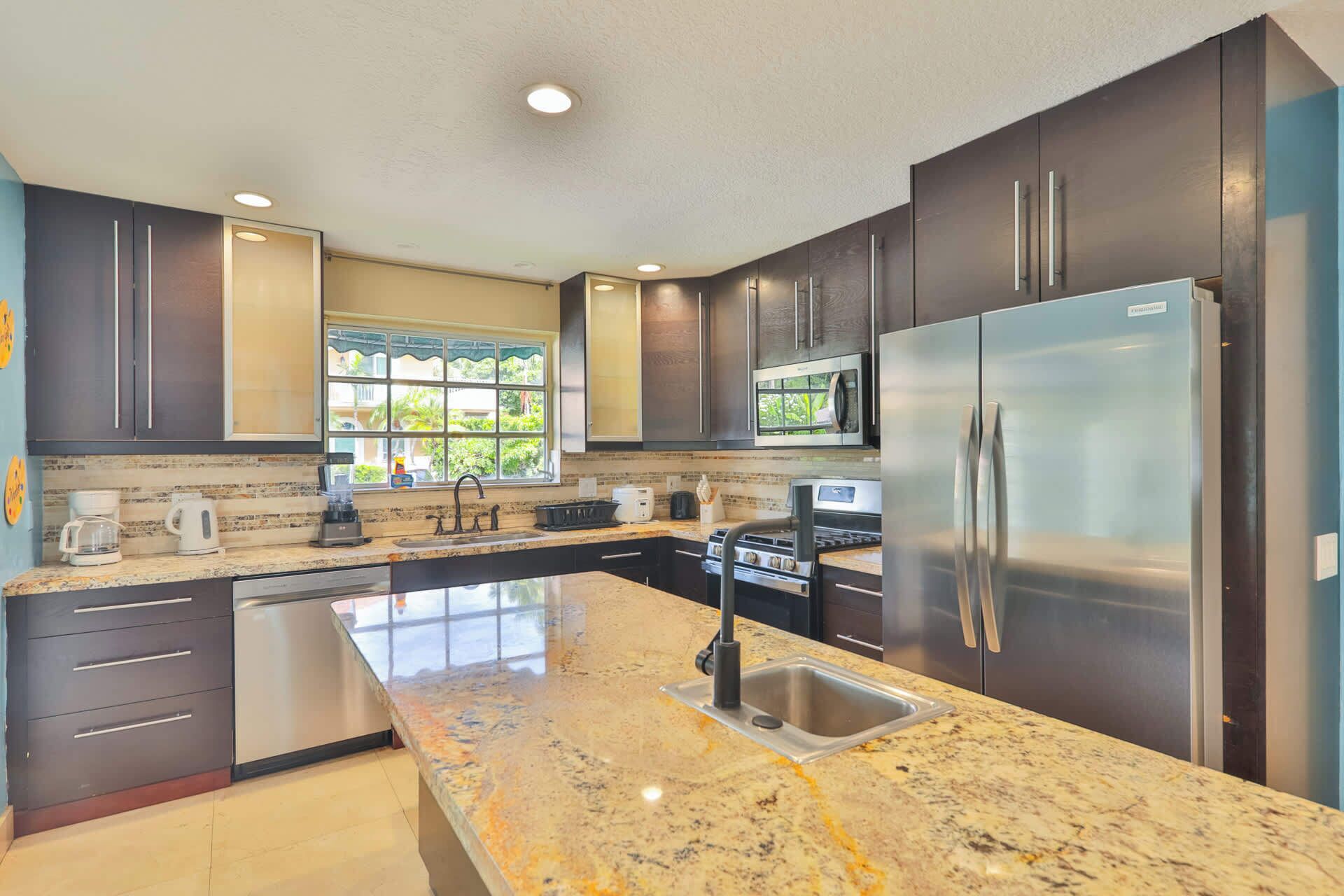 A modern kitchen with dark cabinets, stainless steel appliances, a granite countertop, and a window providing natural light.