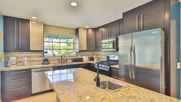 A modern kitchen with dark cabinets, stainless steel appliances, a granite countertop, and a window providing natural light.