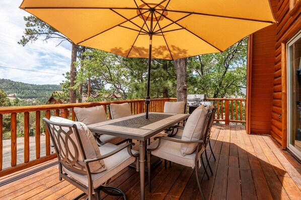Eine Holzterrasse mit Tisch, Stühlen, einem Sonnenschirm und einem Grill.