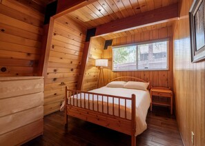 Ein Schlafzimmer einer Holzhütte mit Bett, Nachttisch, Lampe und Fenster.