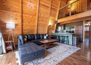 Ein Holzblockhaus-Interieur mit einem Ecksofa, einem Esstisch und einer Küchenzeile.