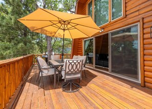 Eine Holzterrasse mit Tisch und Stühlen, einem großen Sonnenschirm und einer Schiebetür.