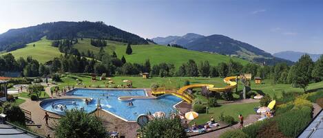 A swimming pool with a water slide and a view of green hills in the background.