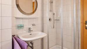 A bathroom with a white sink, a mirror, a shower with a glass door, and a wooden door. - Cozy Holiday Apartment Near the ski Slope (Maria Alm am Steinernen Meer)