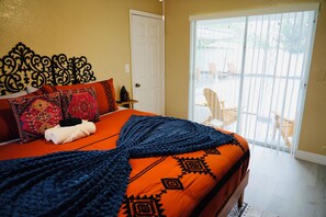 Camera da letto con un letto, cuscini, una coperta, una porta e vista attraverso una porta scorrevole in vetro.
