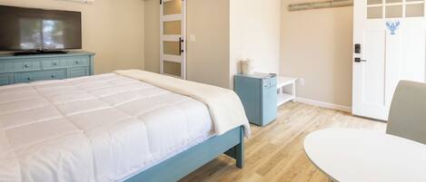 A bedroom with a bed, a TV, a desk, a chair, and a door.