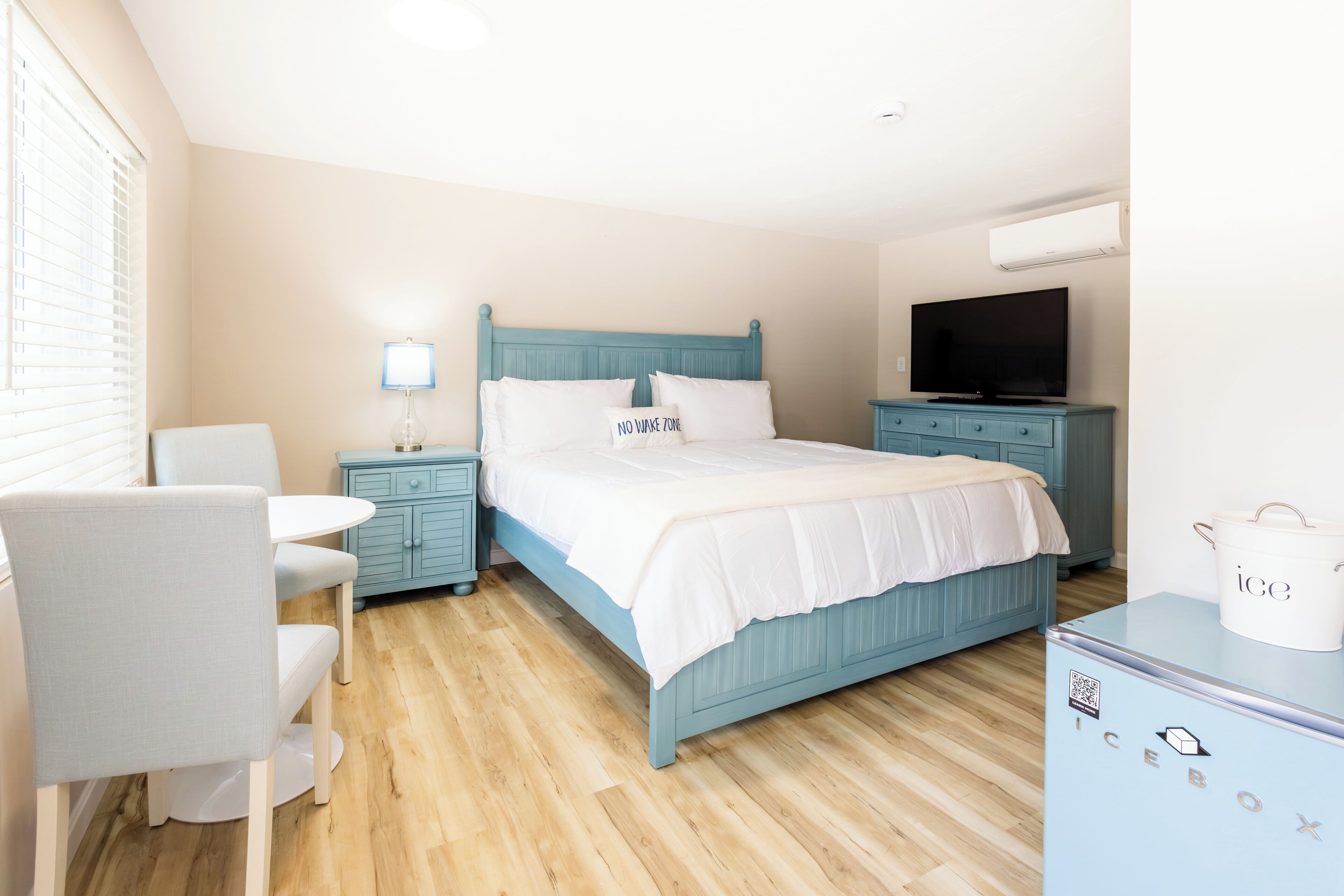 Un dormitorio con cama, mesita de noche, lámpara, televisor y refrigerador.