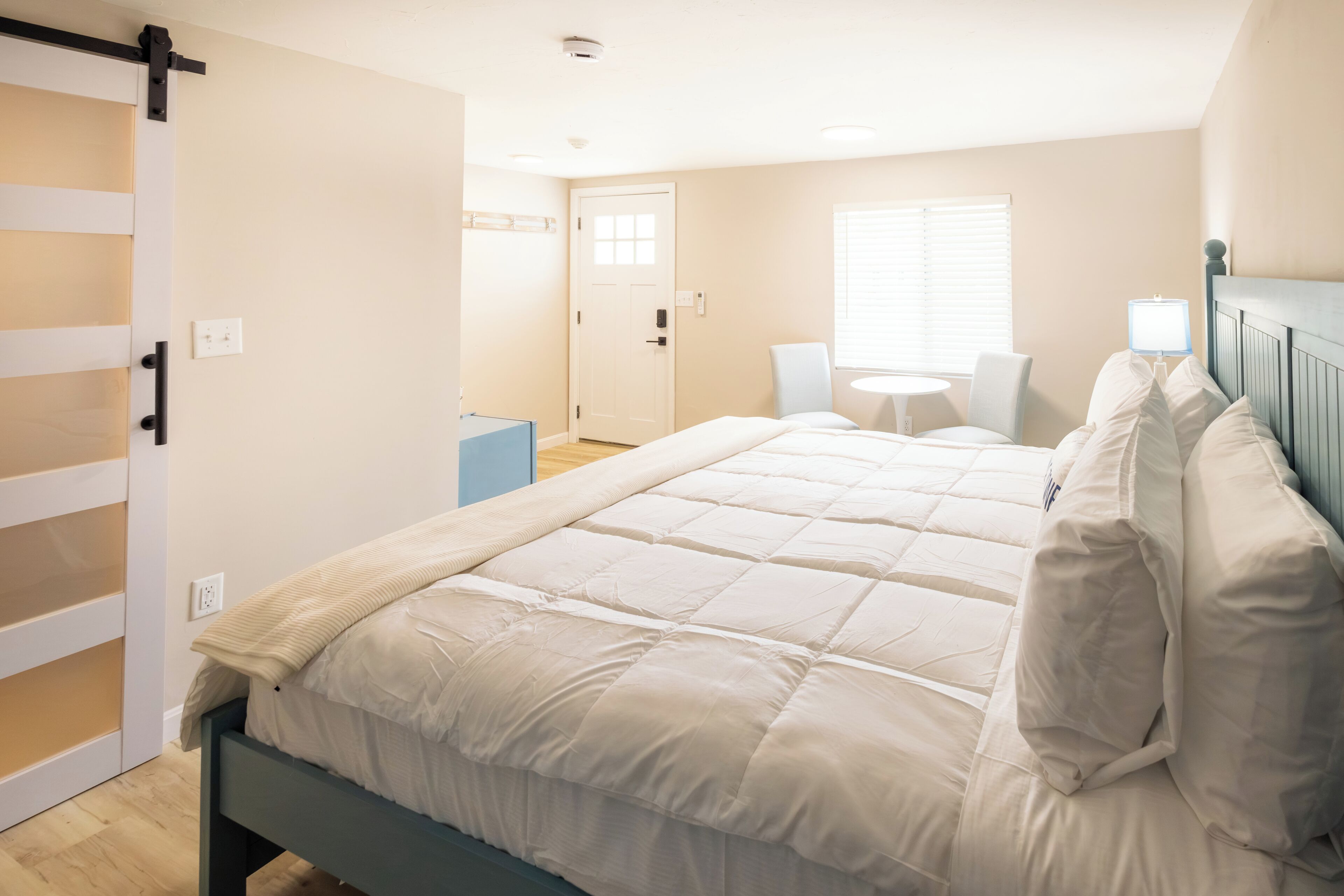 A bedroom with a bed, a chair, a small table, and a door.
