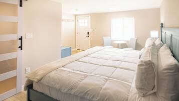A bedroom with a bed, a chair, a small table, and a door.