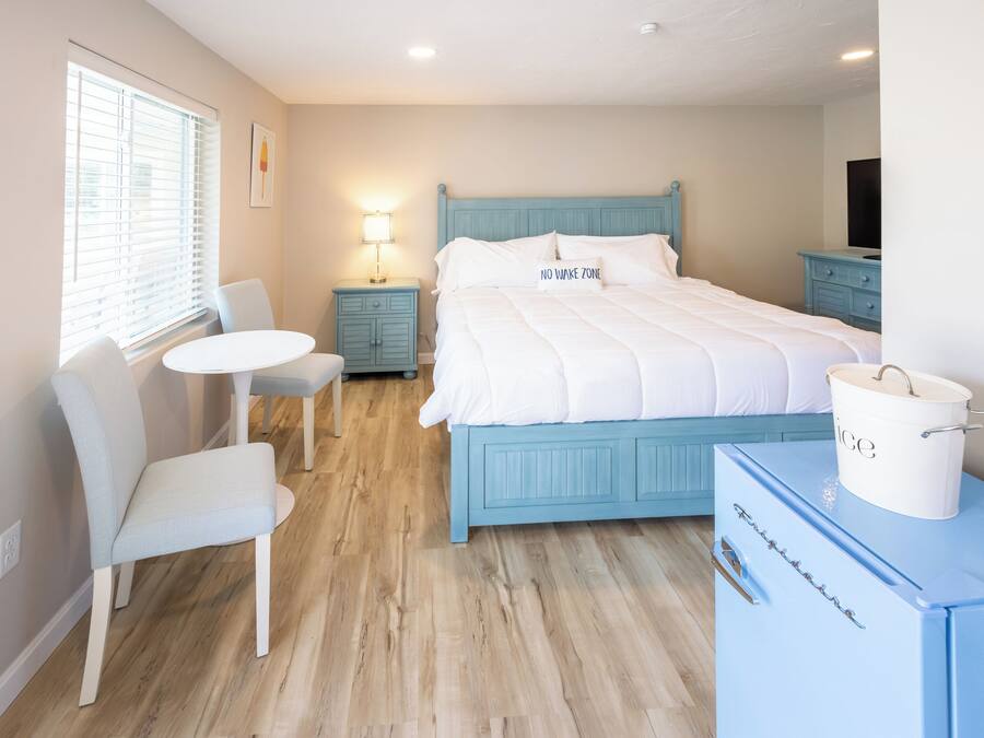 A bedroom with a bed, a nightstand, a lamp, a chair, a small table, and a dresser.