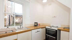 Eine kompakte Küche mit Geschirrspüler, Backofen und Fenster mit Blick auf eine Ziegelhausfassade.