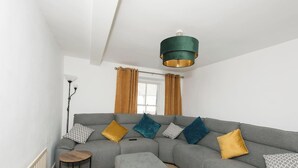 Ein modernes Wohnzimmer mit einem grauen Sofa, mehreren Kissen, einem kleinen runden Tisch und einer Pendelleuchte.