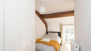 Ein Schlafzimmer mit einem Bett, einem Fenster mit Vorhängen, einem Heizkörper und einem weißen Kleiderschrank.