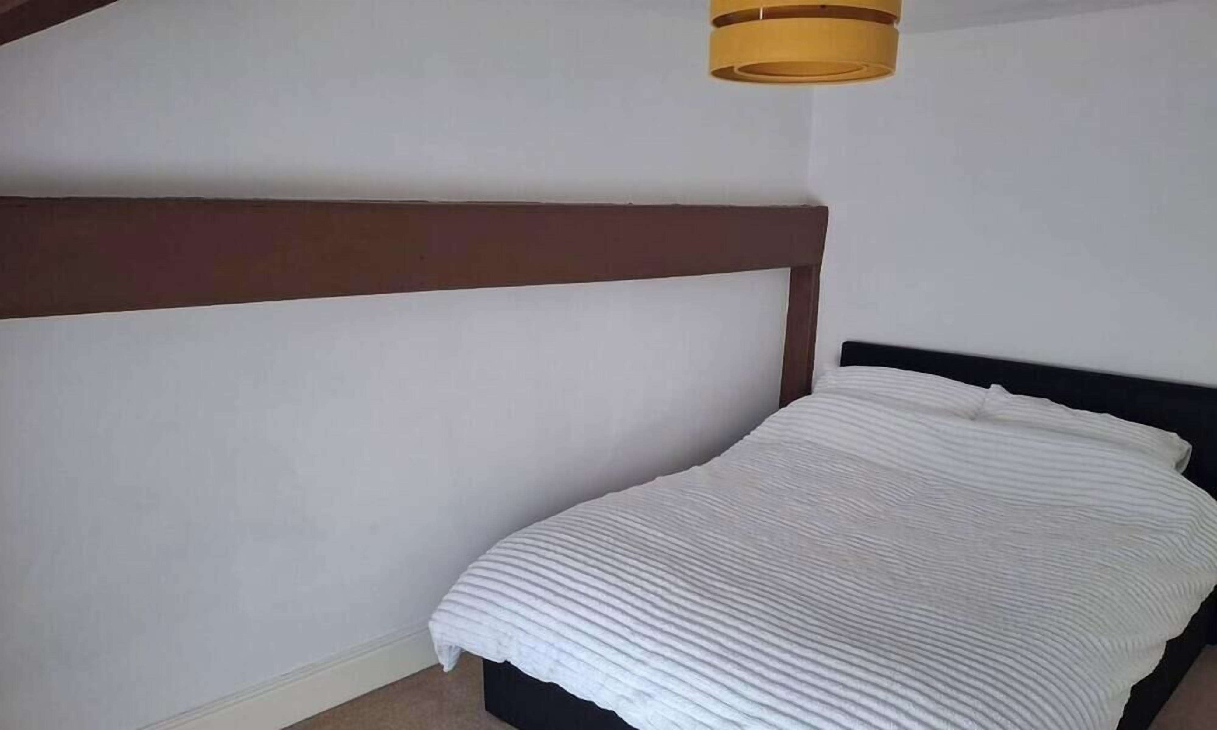 Un dormitorio con cama, cabecera de madera y lámpara en el techo.