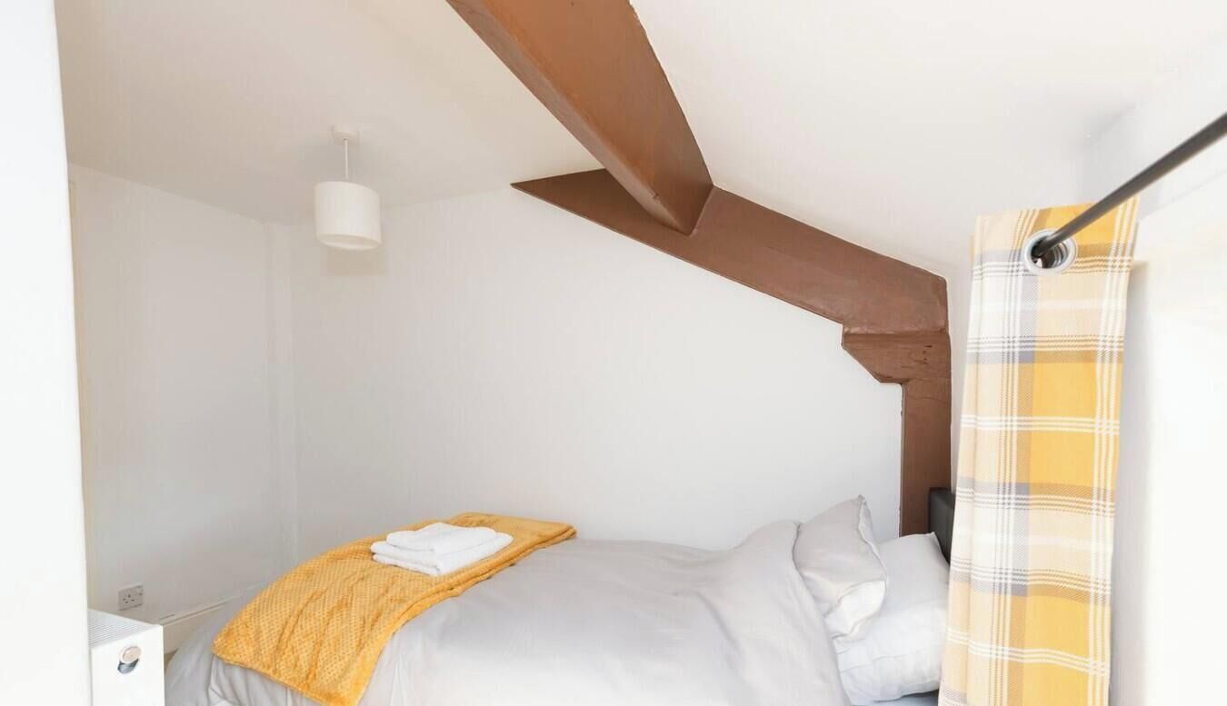 A bedroom with a bed, a bedside table, a lamp, and a window with a curtain.