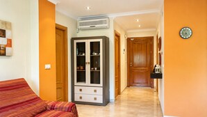 Una habitación con sofá, un armario, un equipo de aire acondicionado y un pasillo que conduce a una puerta.