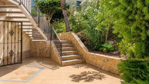 Una escalera de piedra conduce a un balcón, rodeado de exuberante vegetación y una palmera.