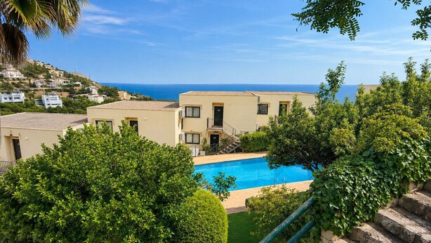 Una piscina rodeada de vegetación, una escalera y edificios con vistas al mar.