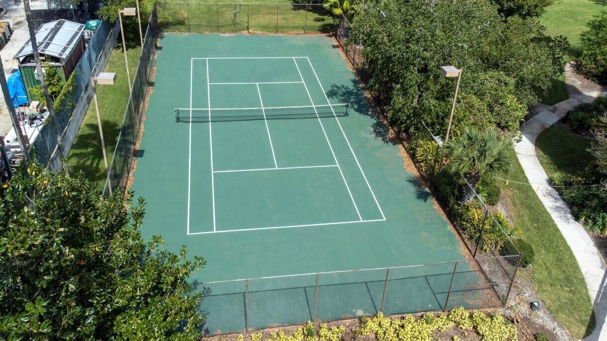 An outdoor tennis court surrounded by trees and a pathway.