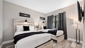 A bedroom with two beds, a window with curtains, a flat-screen TV, and a wall-mounted artwork. - 2BR Suite at The Enclavenear Universal (Orlando)