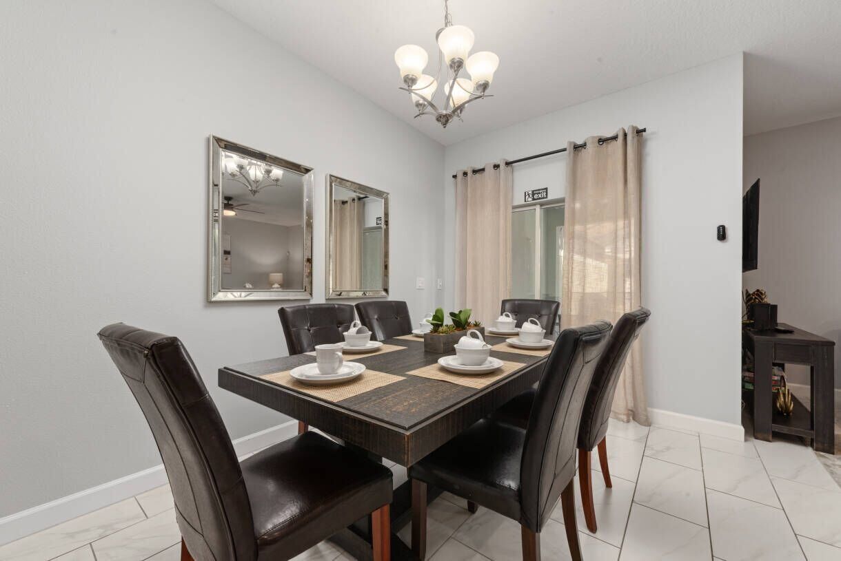 A dining area with a rectangular table, six chairs, two wall mirrors, a chandelier, and a small plant on the table.