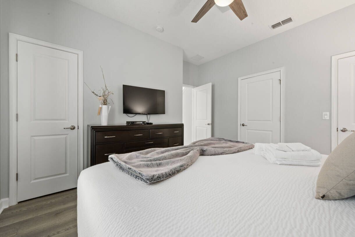 A bedroom with a bed, a television, a dresser, and two doors.