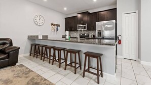 A modern kitchen with dark cabinets, stainless steel appliances, and a bar stool seating area. - Storey Lake Home Pool 15min to Disney (Kissimmee)