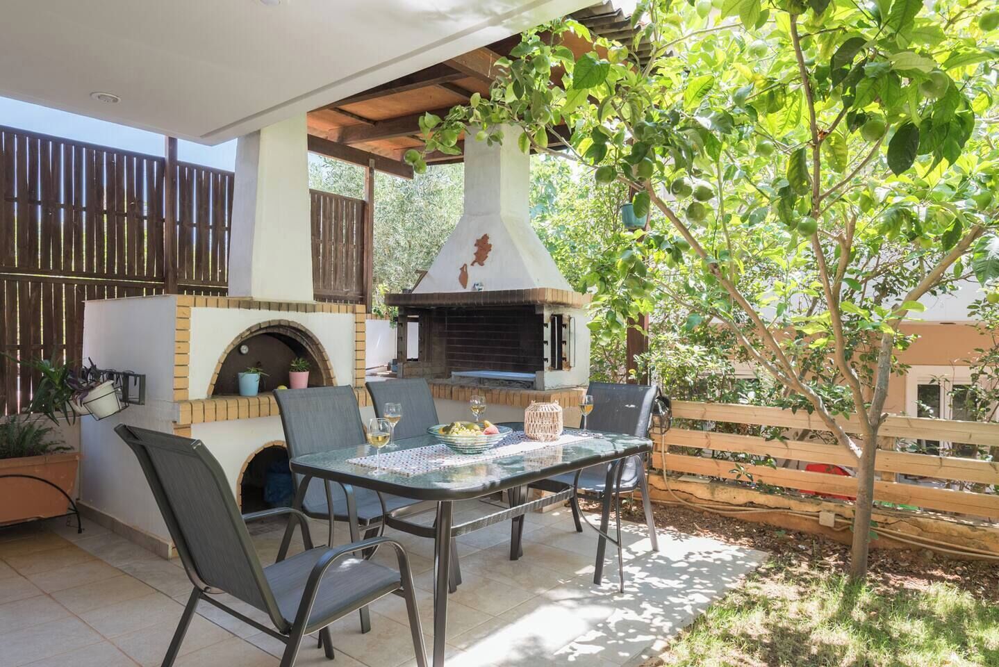 An outdoor patio with a brick oven, dining table, chairs, and potted plants.